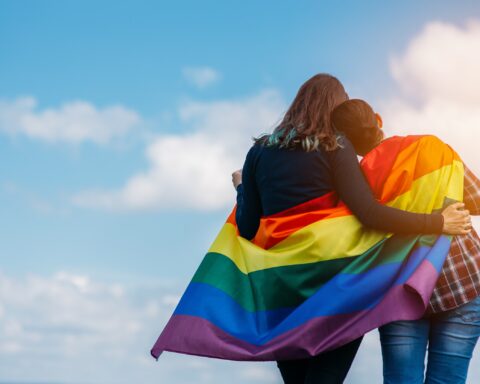 lgbtq lake district - Lesbian couple hugging outdoors. LGBT rainbow flag.