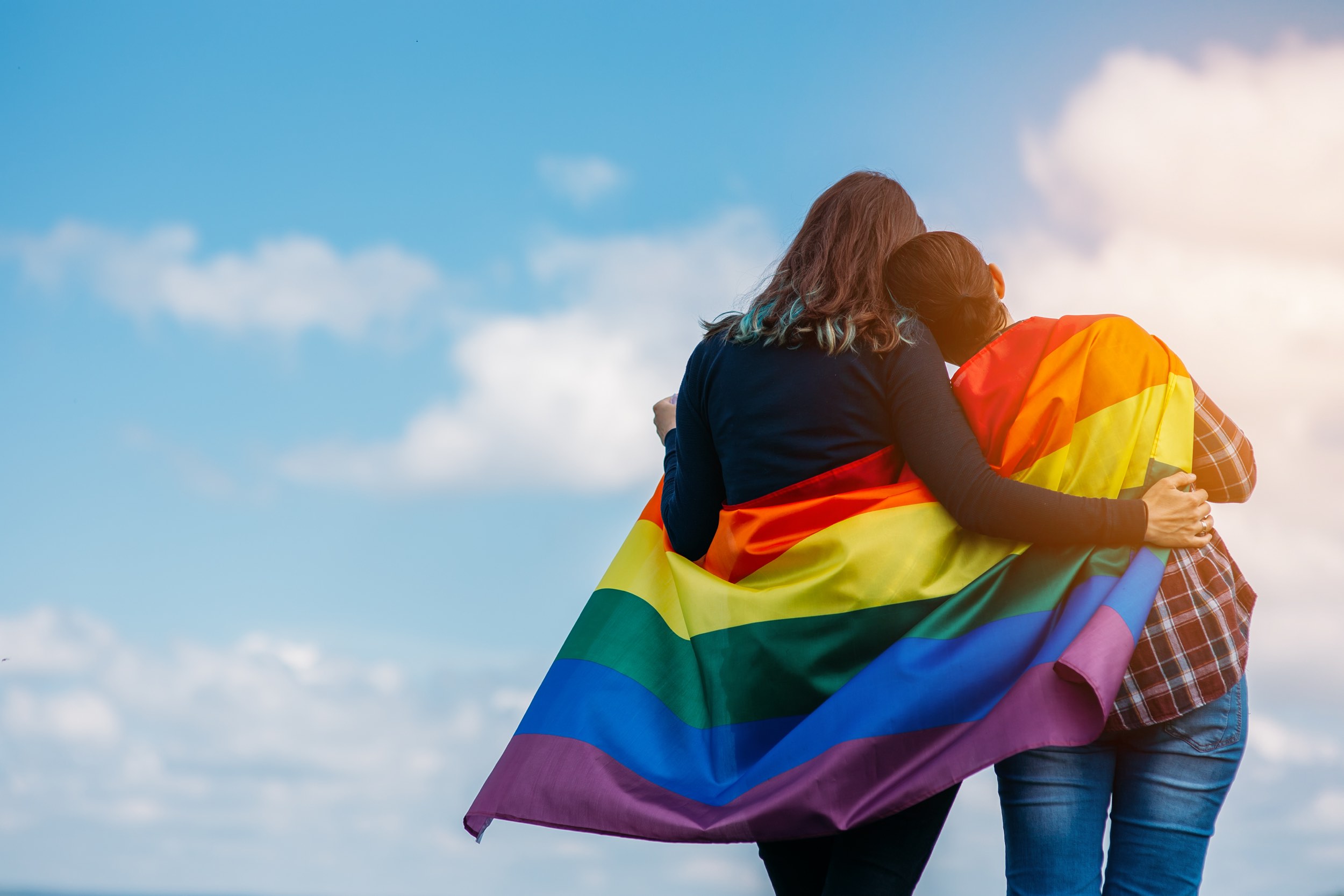 lgbtq lake district - Lesbian couple hugging outdoors. LGBT rainbow flag.